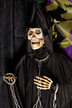 Halloween, doll Death in a black hoodie and a hood on the head with metal chains on the neck and arms.