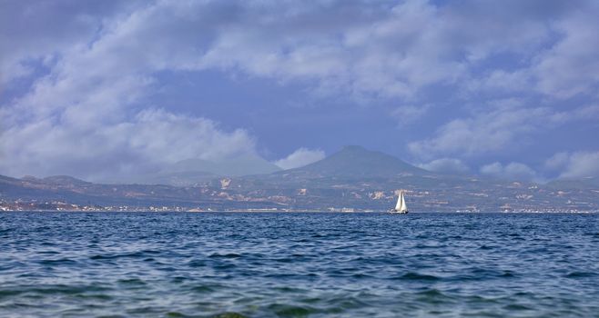 Silhouette of a sailing yacht on the horizon against the backdrop of Mount Acropolis in Corinth in the morning haze.