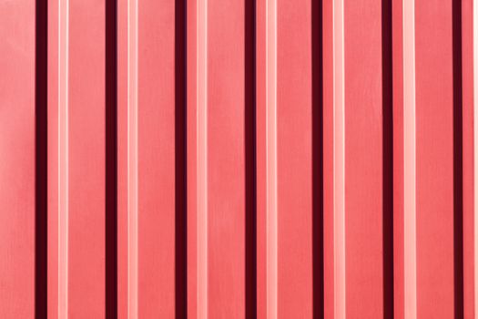 Red metal fence made of corrugated steel sheet with vertical guides and a soft sunny gradient.