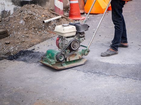 Worker use vibratory plate compactor compacting asphalt at road repair