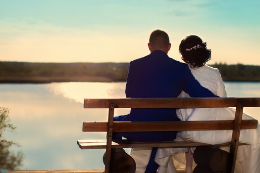 The bride and groom sit on a bench and look at the river. Bride and groom
