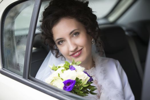 Portrait of a bride in a car with a bouquet