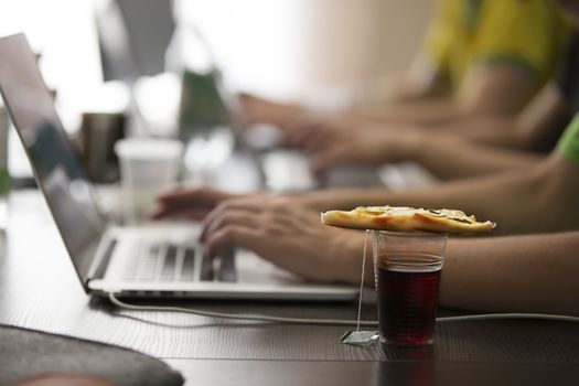 A plastic glass of tea and a piece of pizza on the table at the programmers. Lunch programmer.