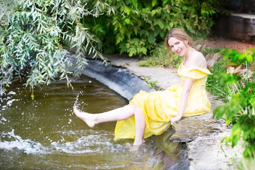 Russia, Moscow, Izmaylovsky Park, August 27, 2017. International Photo Festival.A cheerful girl by the water. A girl by the lake splashes her feet with water.