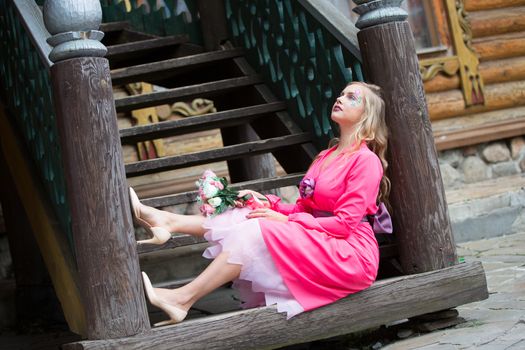 A gorgeous blonde with a bouquet sits on the steps. The girl dreams of love