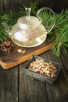 Tea pot of herbal tea with pine buds on wooden background, vertical image