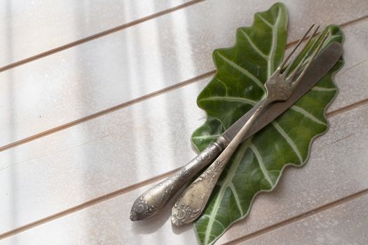 Antique silverware and fresh green leaf on light wooden table