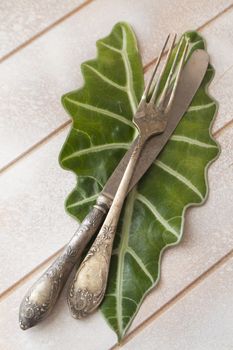 Rustic table place setting, top view, knife and fork on a leaf, vertical image