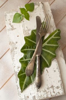 Fork and knife on wooden board with fresh basil leaves, vertical image