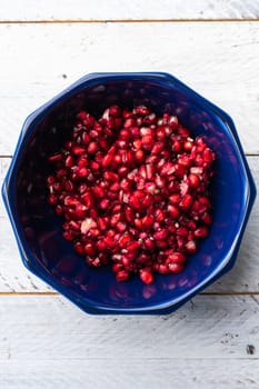 Ripe pomegranate grains in a dark blue bowl placed in the center on a light blue table. Top view