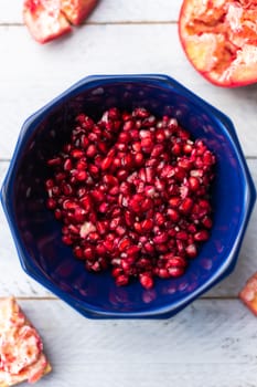 Ripe pomegranate grains with the shell around, in a dark blue bowl placed in the center of a light blue table. Top view