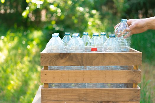 Reuse of plastic bottles recycling concept. Man's hand leaving a plastic bottle in a recycled wooden box with plastic water bottles without a cap with nice sunset in the garden