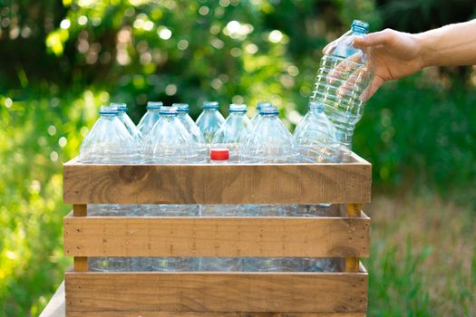 Reuse of plastic bottles recycling concept. Man's hand leaving a plastic bottle in a recycled wooden box with plastic water bottles without a cap with nice sunset in the garden