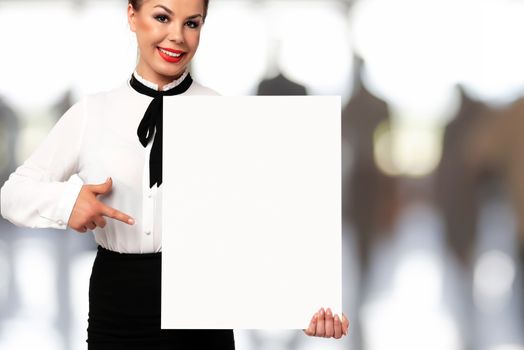 Beautiful business woman smiling and holding a white sign board with copy space for advertising and text on a blurred background of the office.