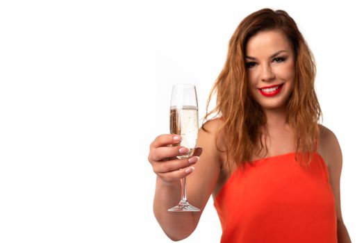 Celebration event concept - young and attractive woman in an orange dress with perfect fingernails holds a glass of champagne or wine and smiling on a white background (copy space).