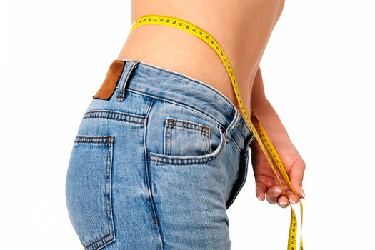 Healthy lifestyle concept - woman in blue jeans measures her perfect waistline with a measuring tape in close-up