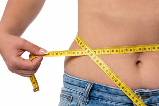 Healthy lifestyle concept - woman in blue jeans measures her waistline with a measuring tape in close-up