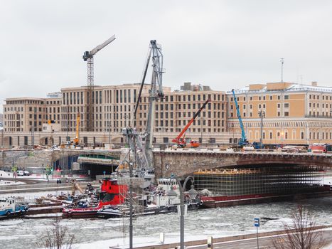 Ships with construction equipment are in Moscow-river under the bridge. Reconstruction of Bolshoy Moskvoretsky Bridge. Winter cloudy day in Moscow, Russia.