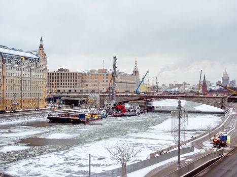 Ships with construction equipment are in Moscow-river under the bridge. Reconstruction of Bolshoy Moskvoretsky Bridge. Winter cloudy day in Moscow, Russia.