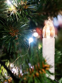 Christmas tree with decorative candle. New Year electric garland with light bulbs.