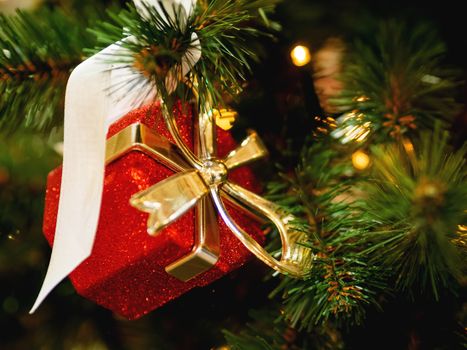 New Year decorative red present box with golden ribbon on Christmas tree. Holiday decorations.