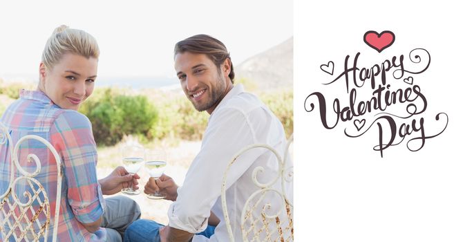 Happy young couple sitting in the garden enjoying wine together against happy valentines day