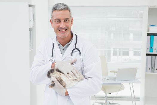 Smiling vet with a rabbit in his arms in medical office