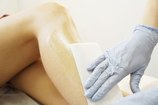 Hair removal from beautiful female legs. Waxing in a beauty salon. Close-up of doctor hands in gloves