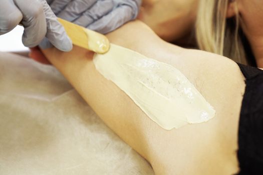Waxing woman armpit with spatula. Salon wax beautician epilation procedure. Waxing female body for hair removal by therapist close up