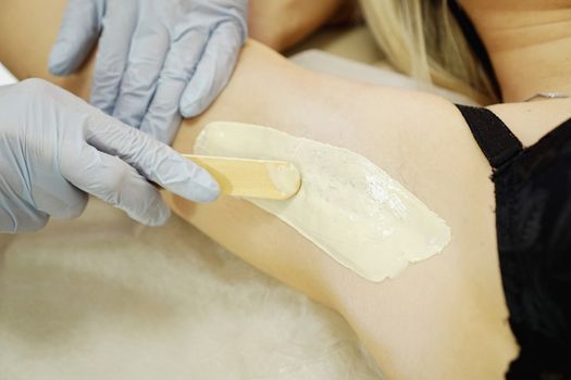 Waxing woman armpit with spatula. Salon wax beautician epilation procedure. Waxing female body for hair removal by therapist close up