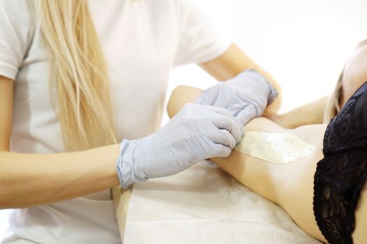 Waxing woman armpit with spatula. Salon wax beautician epilation procedure. Waxing female body for hair removal by therapist close up