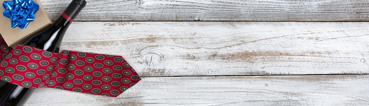 Happy Fathers Day giftbox with a dress tie and bottle of red wine on white rustic wood.  