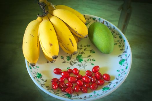 bunch of bananas with a mango and some cherries arranged in a beautiful designed plate for serving