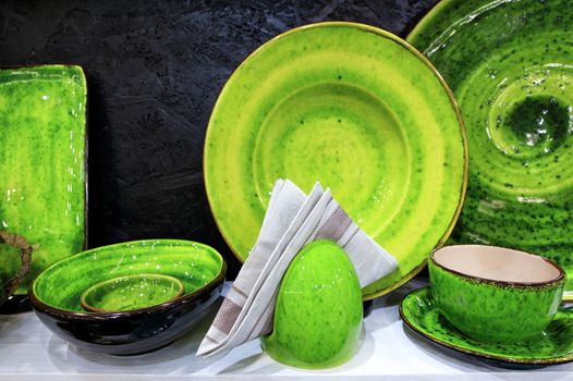 A flannel napkin on the background of a collection of beautiful handmade ceramic dishes of various capacities, covered with bright green glaze.