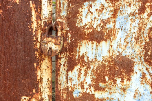 An old rusty door lock and an old metal sheet with rust texture and weathered aged peeling paint.