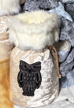 Large New Year's beige shiny gift bag with a fur collar and a gray embroidered owl on it under a decorative gray Christmas tree.
