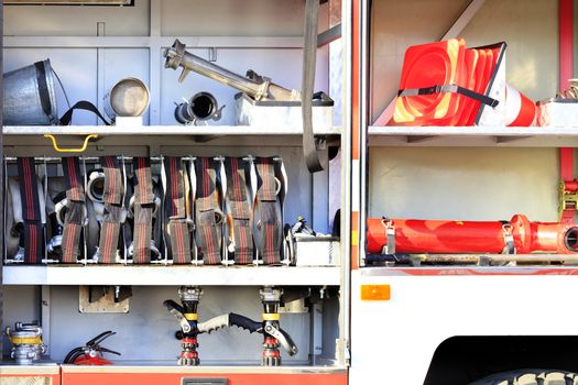 Fire hoses, valves, cranes, road cones, hydrants and a galvanized metal bucket are located in the cargo compartment of an equipped fire truck.