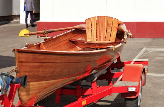 Wooden, bright beautiful orange canoe parked by a young businessman in front of an office building in a car park.