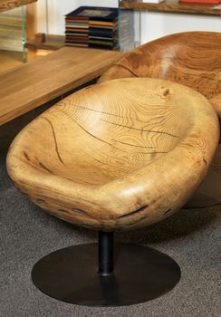 Beautiful stylish modern wooden round chair made of old wood carved from solid wood on a metal leg in modern wooden interior.