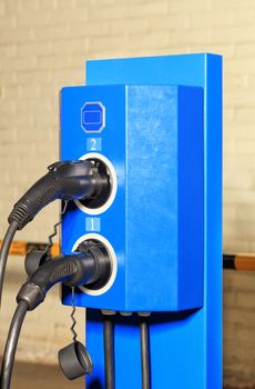 Modern charging station for cars with two nozzles of bright blue in the underground parking.