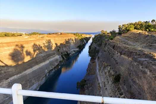 The Corinth Canal on a morning summer day illuminates the bright rising sun in Greece, a view of the Gulf of Corinth from the height of a pedestrian bridge. ??????????? ????????? ????????? ???? ? ?????????? ????? ??????????? ????.