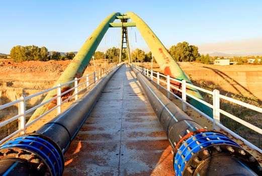 Pedestrian bridge on a bright sunny morning through the Corinth Straits, with engineering communications in the form of polypropylene pipes and iron fittings.