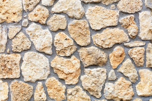 Texture and background of the wall of an old stone made of beige sandstone and coquina n the form of rough homogeneous masonry cobblestone.