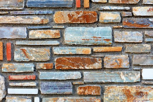 Stone mosaic of brown, blue, gray, white, green, orange stone blocks laid parallel to each other and form a stone background and pattern, surface with cement.