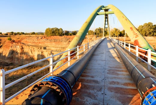 Pedestrian bridge on a bright sunny morning through the Corinth Straits, with engineering communications in the form of polypropylene pipes and iron fittings, image with copy space.