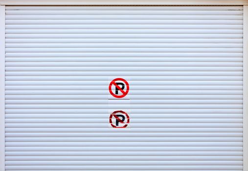 Large white metal shutters, garage doors with an inscribed sticker do not park at the entrance to the car parking. Texture and background closeup, image with copy space.