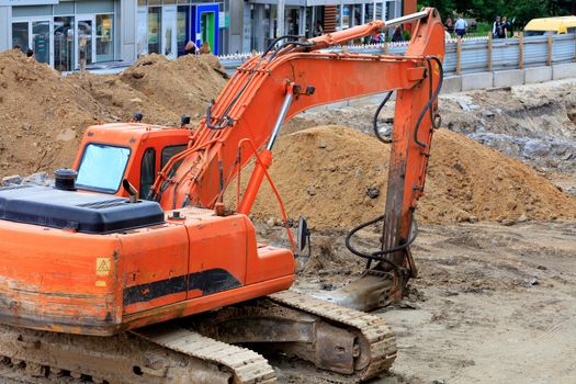 Heavy crawler construction excavator digs trenches for urban utilities at a construction site during road repair on a city street on a summer day, image with copy space.