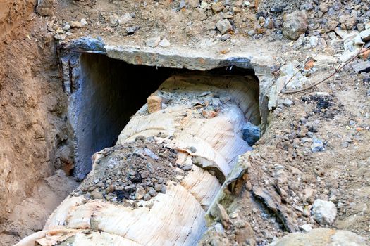 Dug hole in which you can see the pipeline covered with a concrete box and wrapped with insulating wool, the process of repairing water pipes in the heating main.