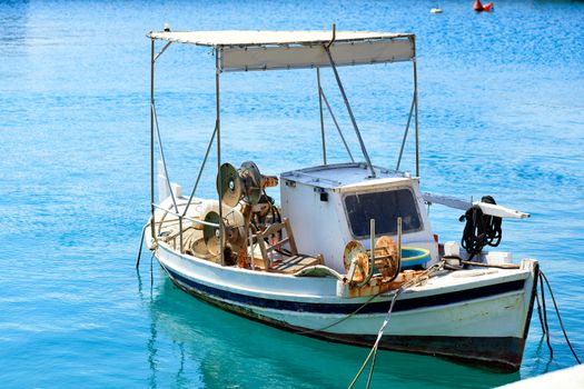 A small old wooden fishing boat with betallic reels for reeling up fishing nets, which sways in motion on the waves at the pier.