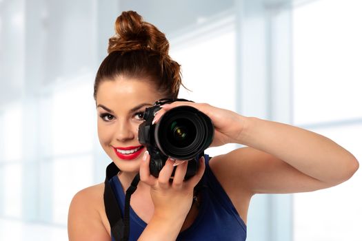 Photographer occupation concept - beautiful and attractive woman holding a professional DSLR camera and smiling in the photo studio